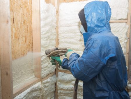 Worker Applying Spray Foam Insulation To Walls Of Attic
