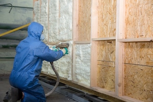 Worker applying spray foam insulation to wall cavity